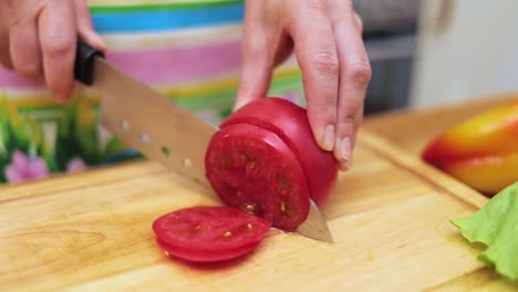 Women's-hands-Housewives-cut-with-a-knife-fresh-tomato-on-the-cutting-Board-of-the-kitchen-table